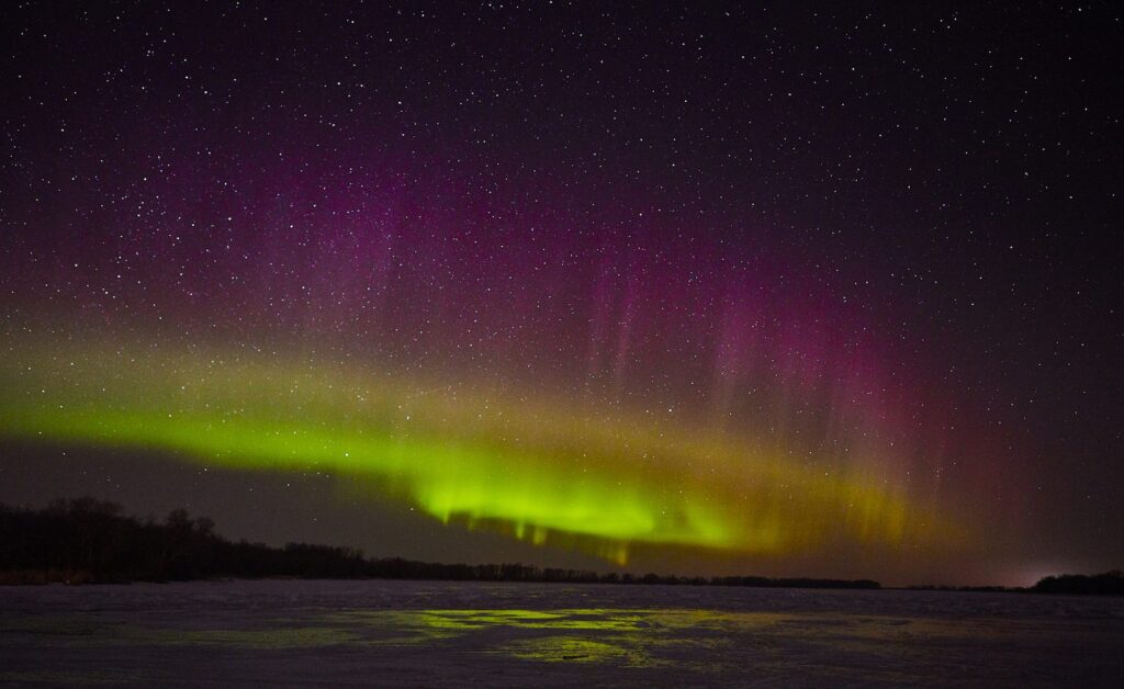 Pink and green aurora over a frozen lake under a starry sky