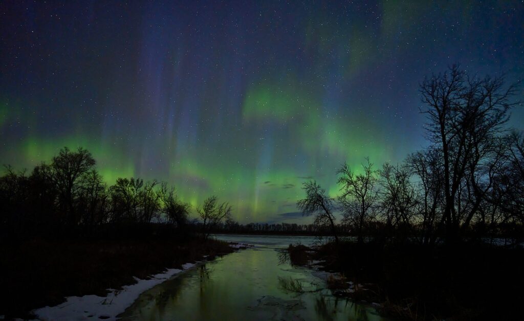 Aurora rays over a river bend with melting snow along the banks