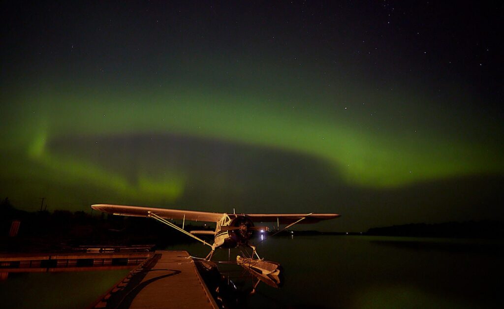 Green aurora arc over a floatplane tied up at a dock