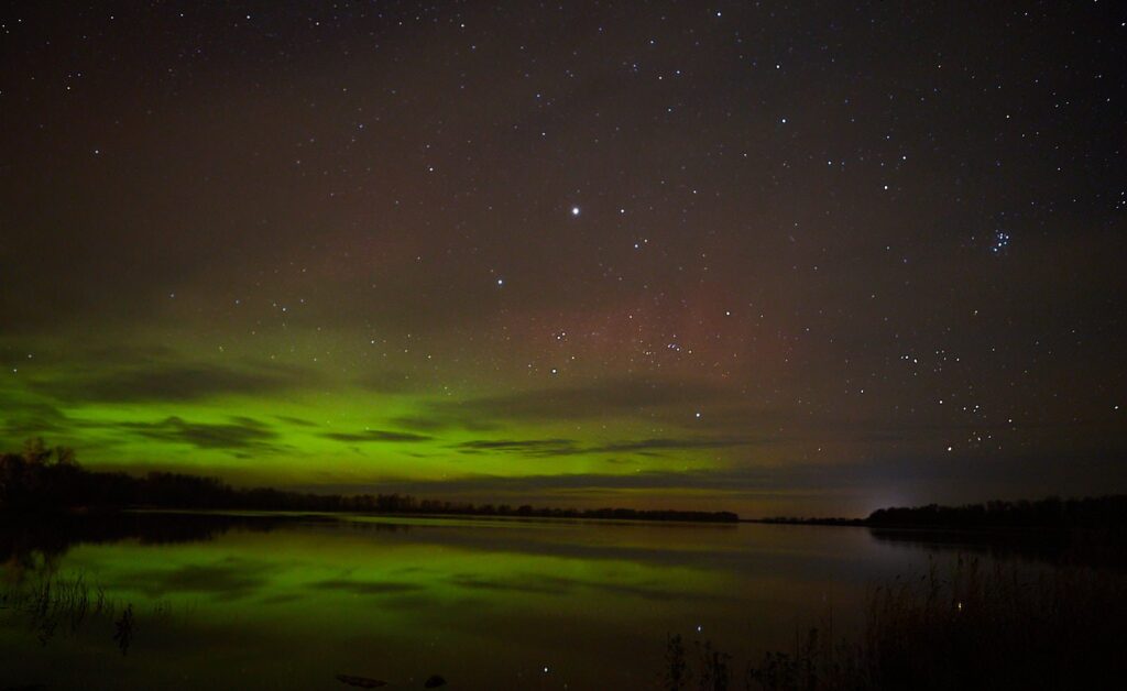 Faint green aurora and stars reflected in dark water