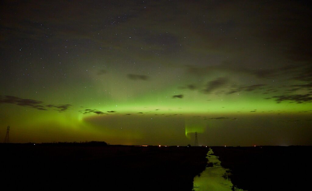 Green aurora band over a field with a ditch leading to the horizon