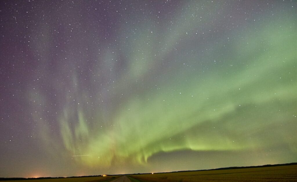 Aurora curtains rippling above a gravel road and a field
