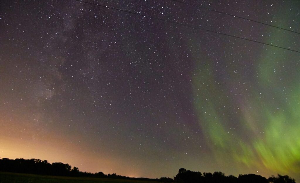 The Milky Way and green aurora over a field with distant town glow