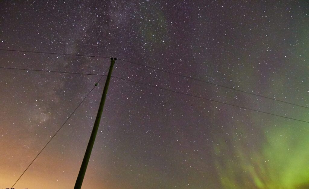 Aurora and the Milky Way beside a leaning power pole