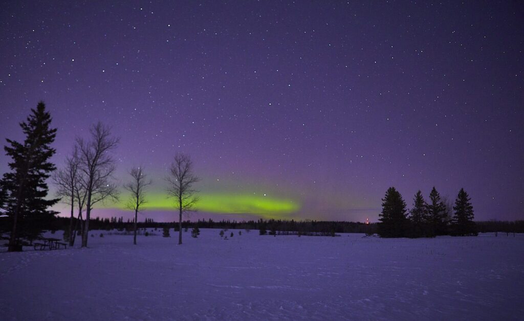 Faint green aurora over a snowy field under a purple sky