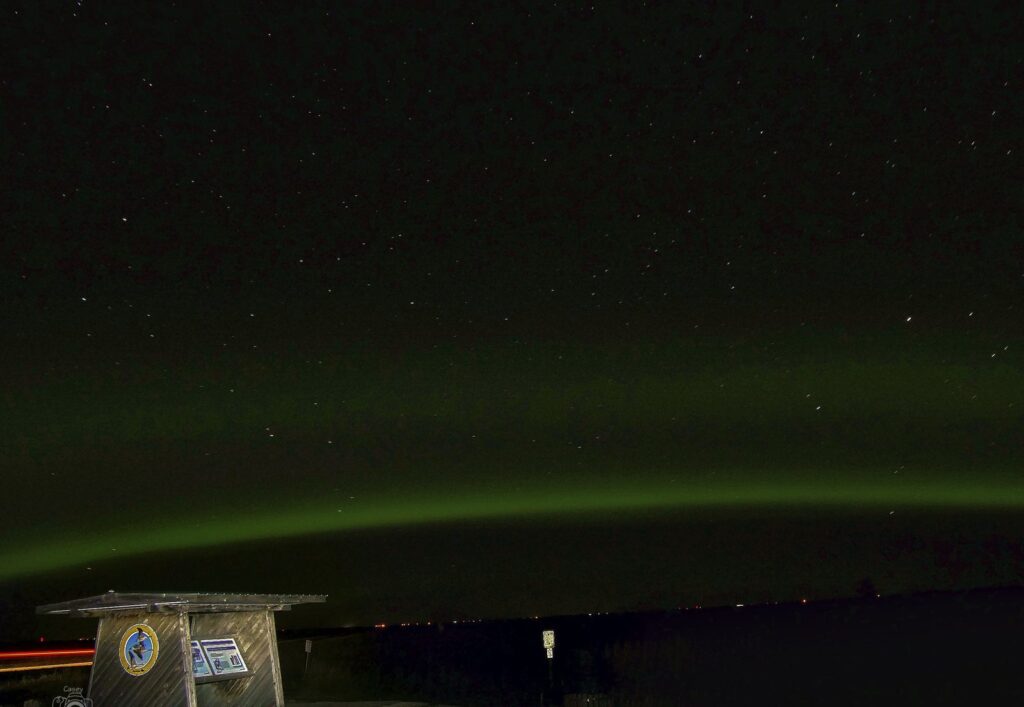 Green aurora arc above a roadside kiosk at night