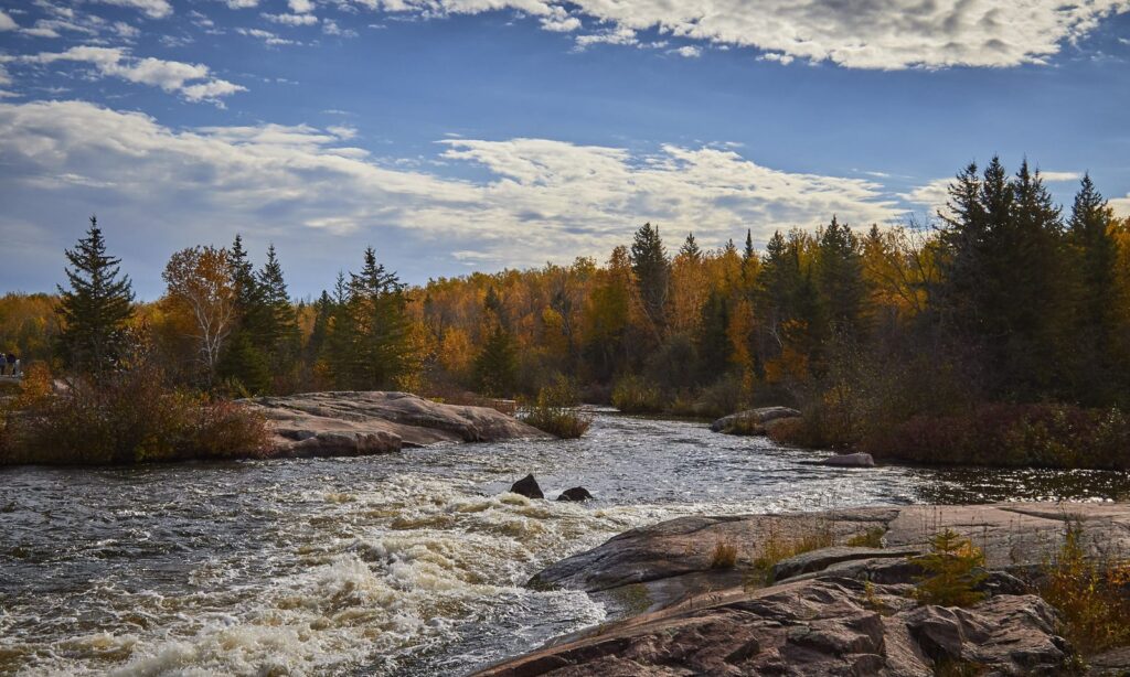 White water running through granite under a blue and cloudy sky