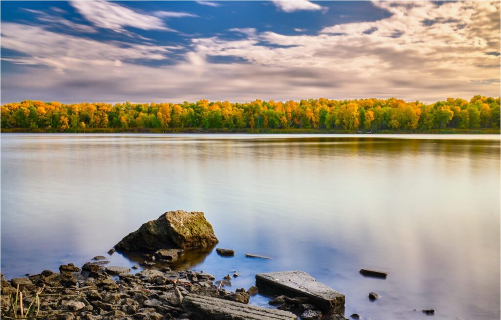 Autumn treeline reflected in a calm lake with rocks in the foreground