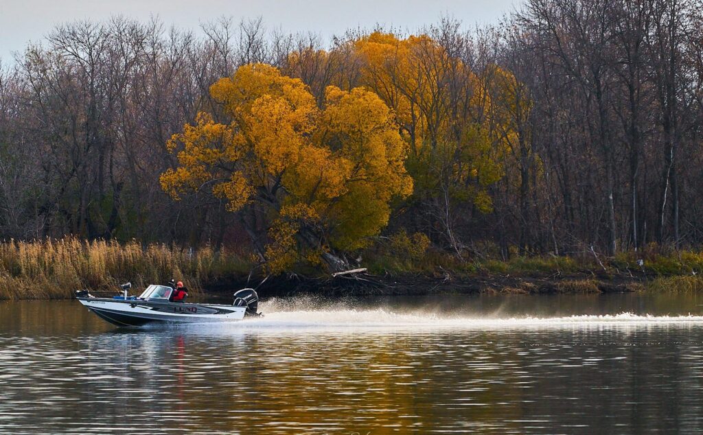 Fishing boat crossing a river in front of autumn trees