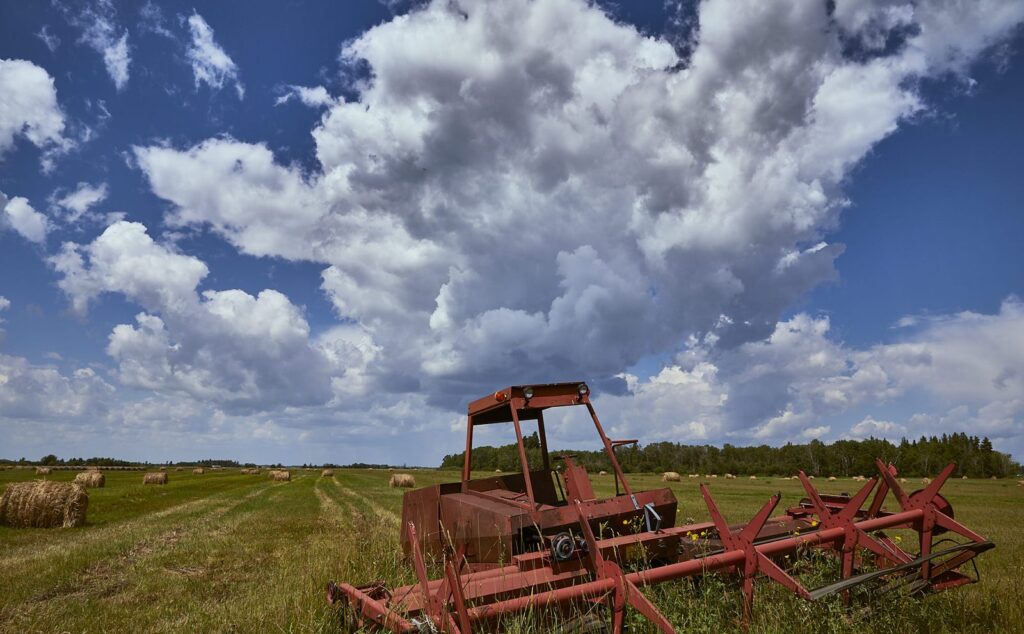 Old red swather in a hayfield under towering cumulus