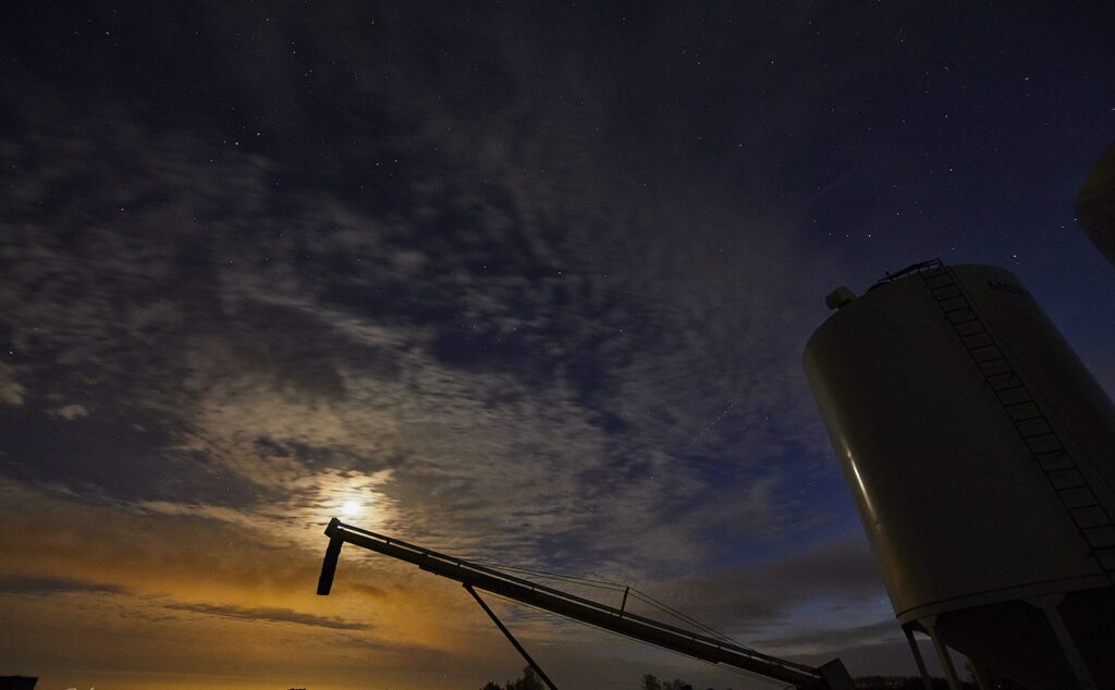 Grain bin and auger silhouetted under a night sky with the moon