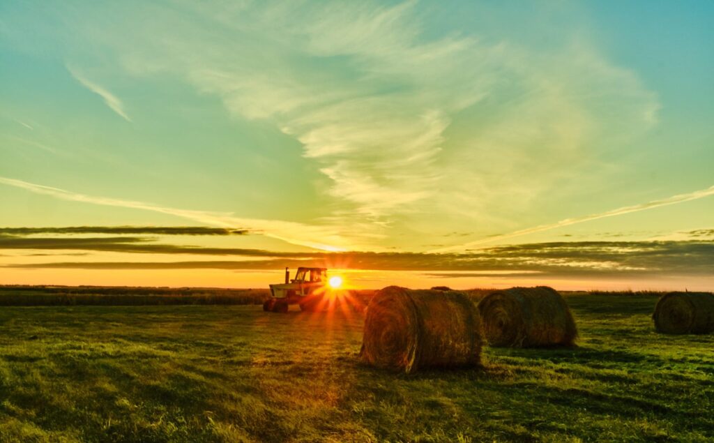 Tractor and round bales at sunrise with the sun starred over the field