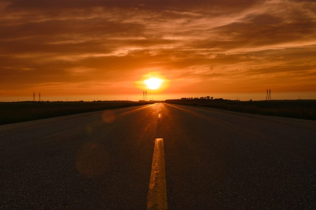 Highway running toward a low sun, with the road shining in the glare