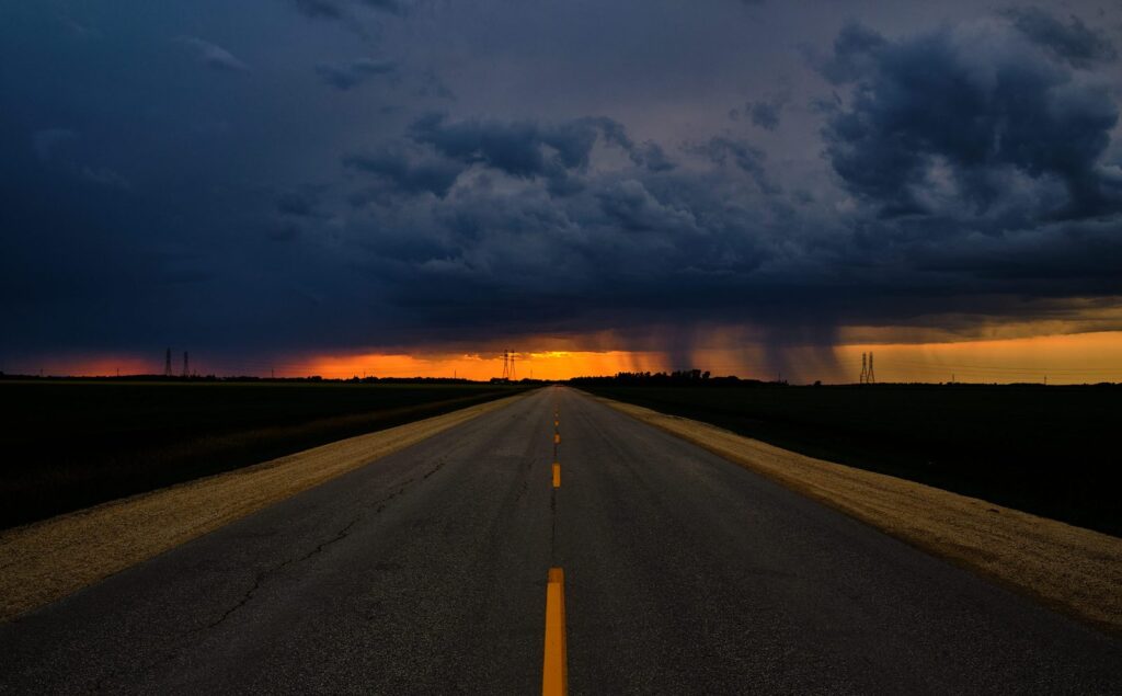 Highway under a dark storm cloud with rain falling on the horizon