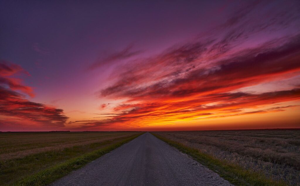 Gravel road under a streaked red and orange sunset sky
