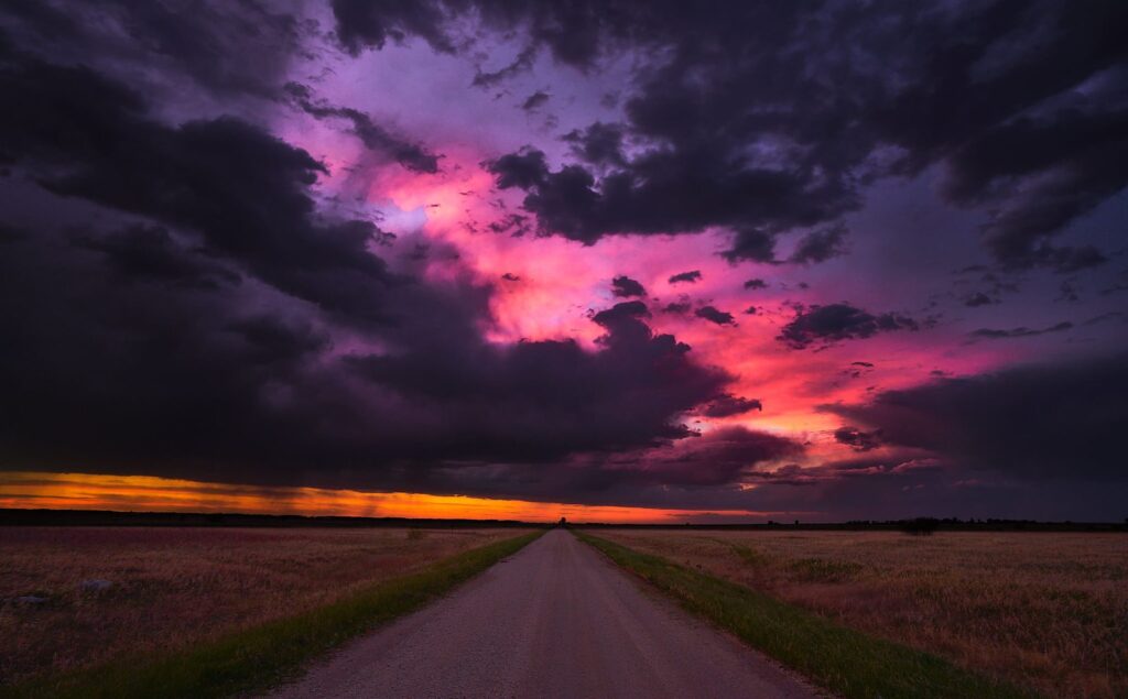 Gravel road beneath a purple and magenta storm cloud at dusk