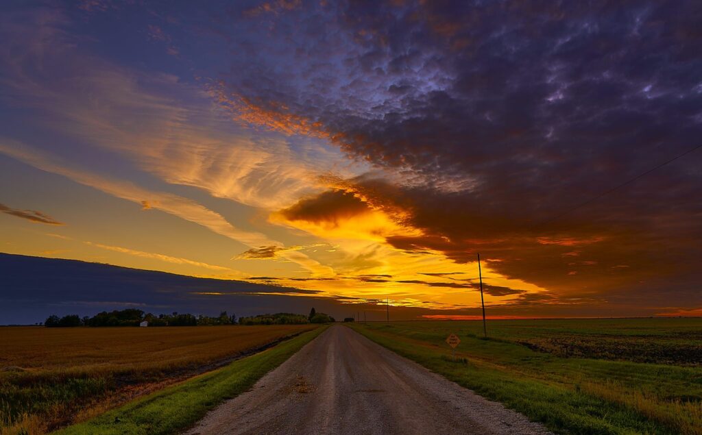 Gravel road beside stubble under an orange sunset and dark cloud