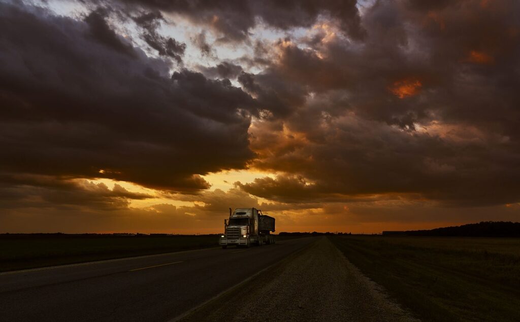 Transport truck on a highway beneath a dramatic orange-lit cloud