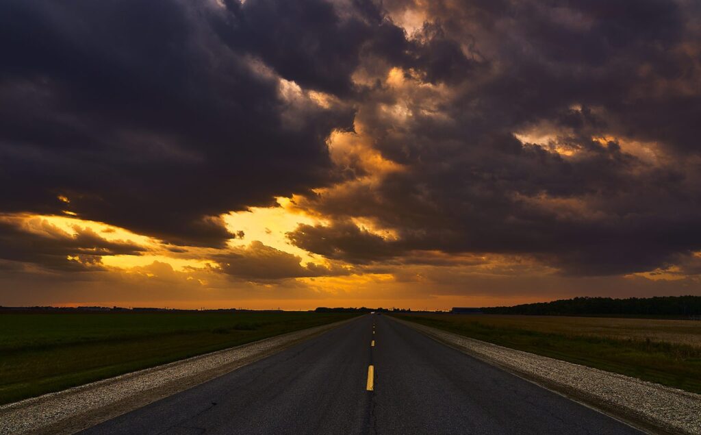 Highway with a yellow centre line beneath breaking storm clouds at sunset