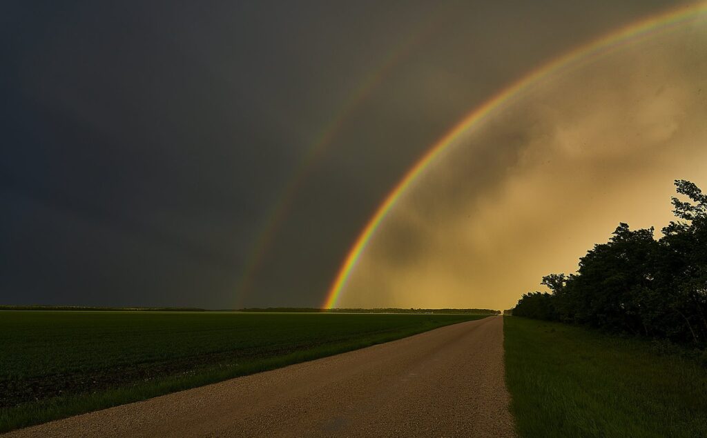 Double rainbow over a gravel road and green field