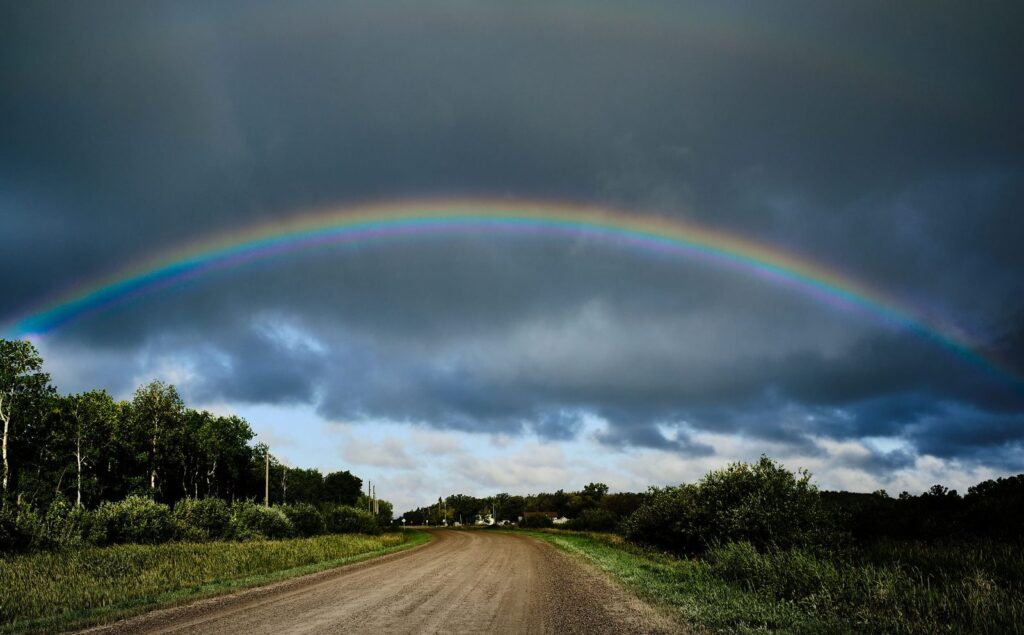Rainbow arching over a gravel road beneath dark cloud