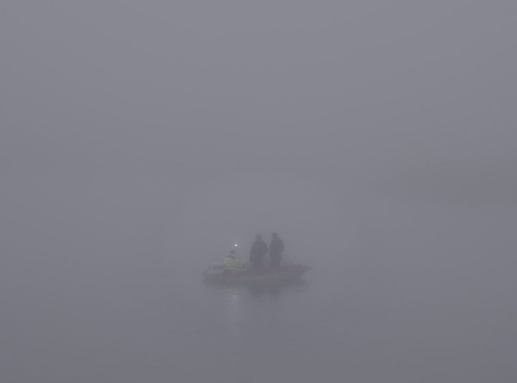 Fishermen in a boat with a small light, glowing in thick fog