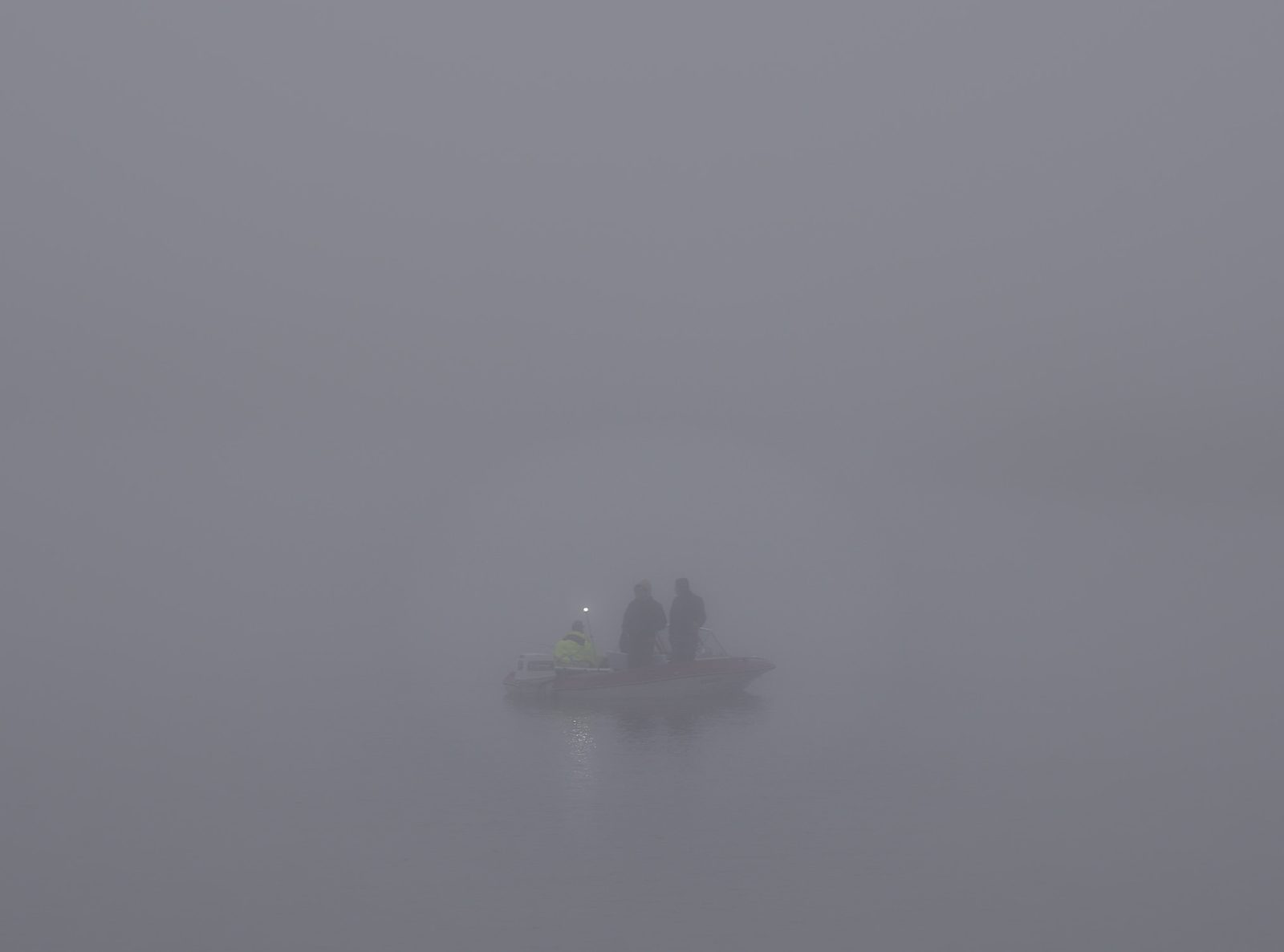 Fishermen in a boat with a small light, glowing in thick fog