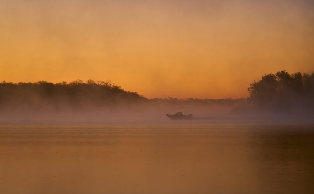 Boat crossing a river under an orange sunrise mist