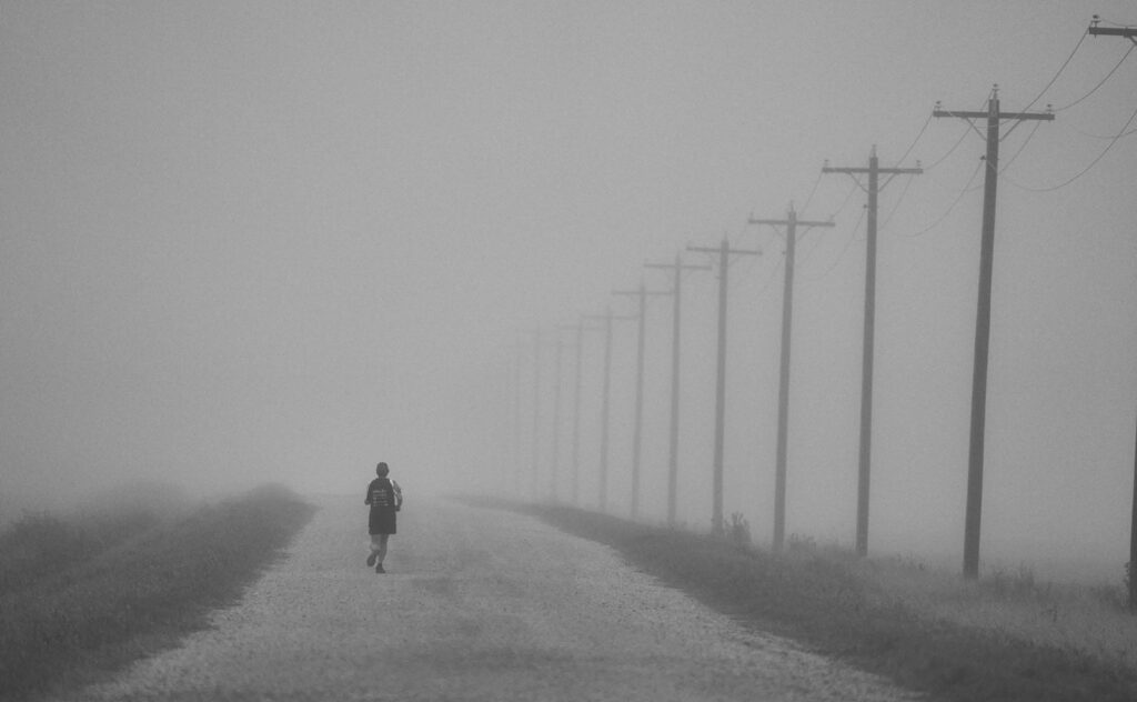 Runner on a gravel road beside power poles in fog