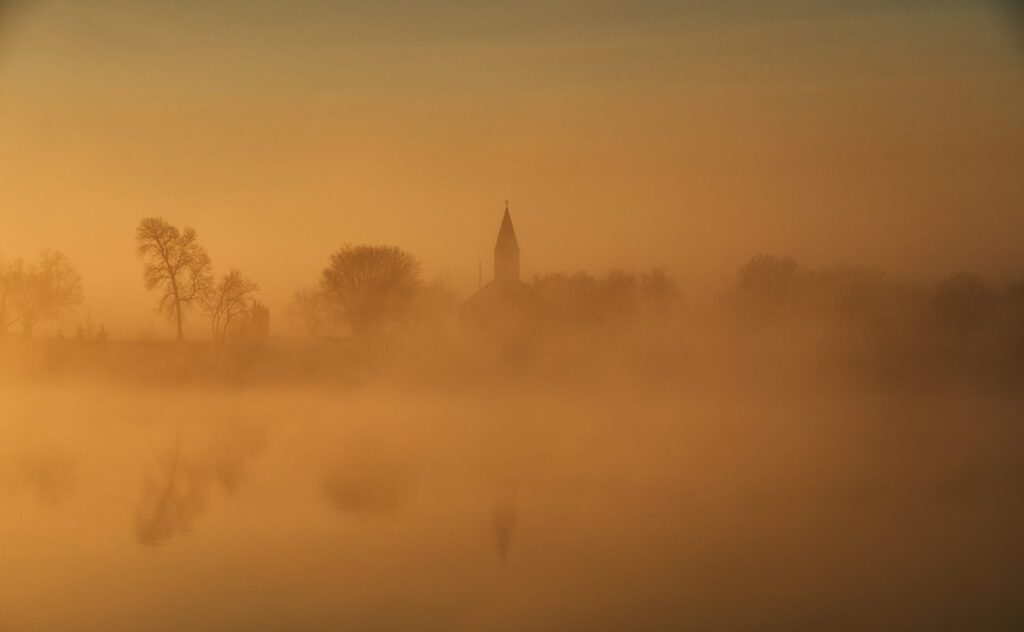 Orange river fog at dawn with a church steeple and reflections