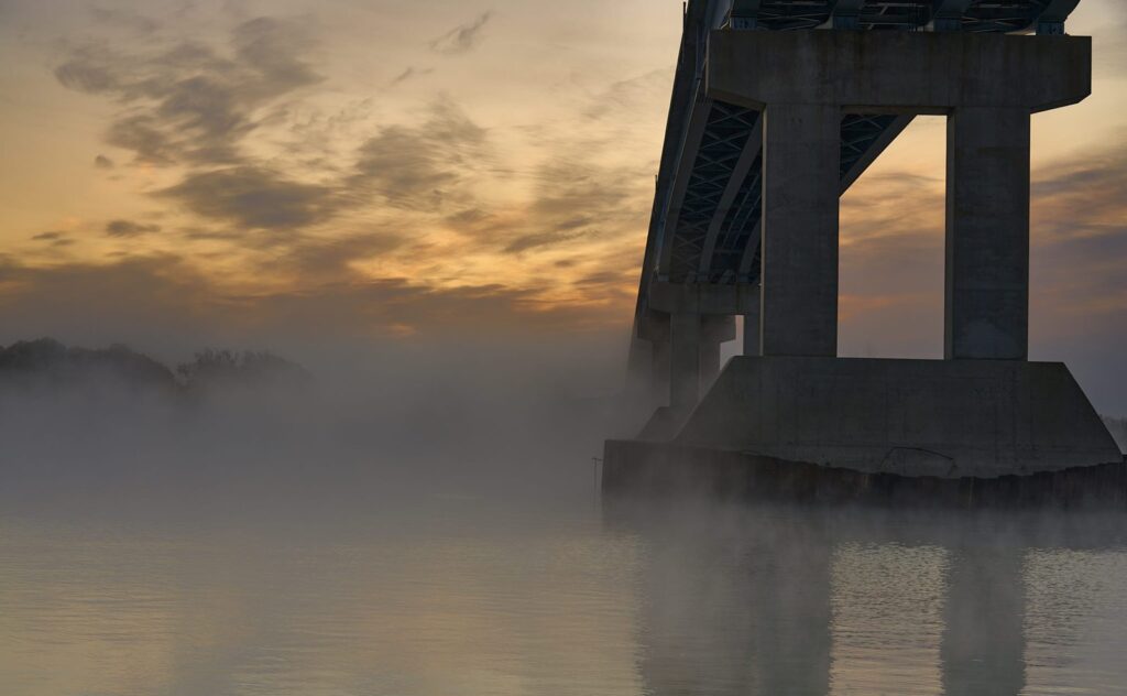 Bridge pier rising out of river fog at sunrise