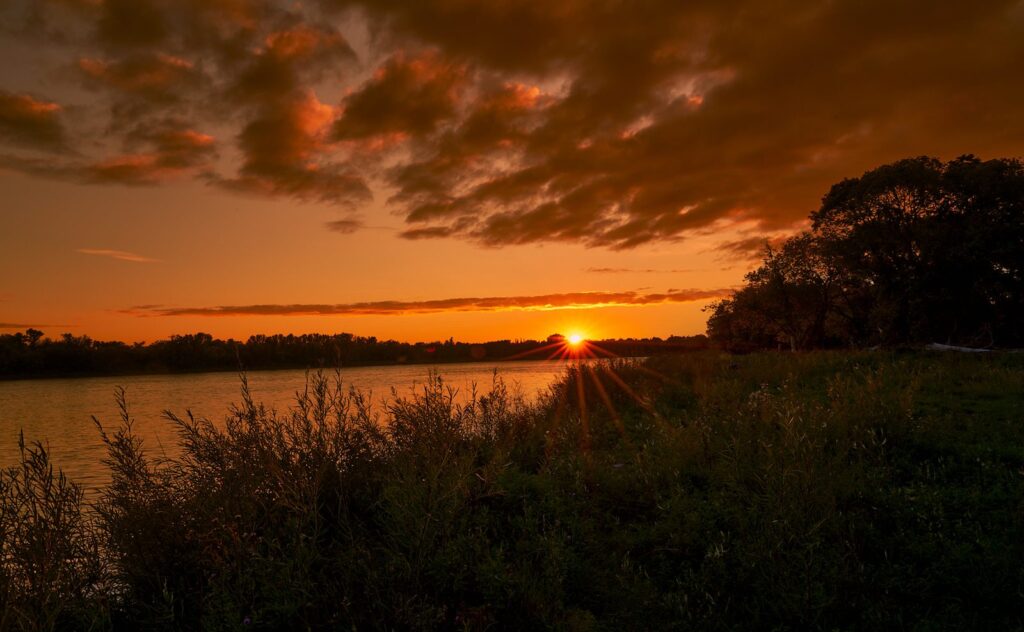 Sunset over a river bank with the sun just above the horizon