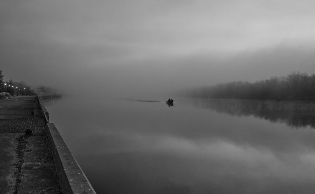 Misty waterfront and a distant boat, in black and white