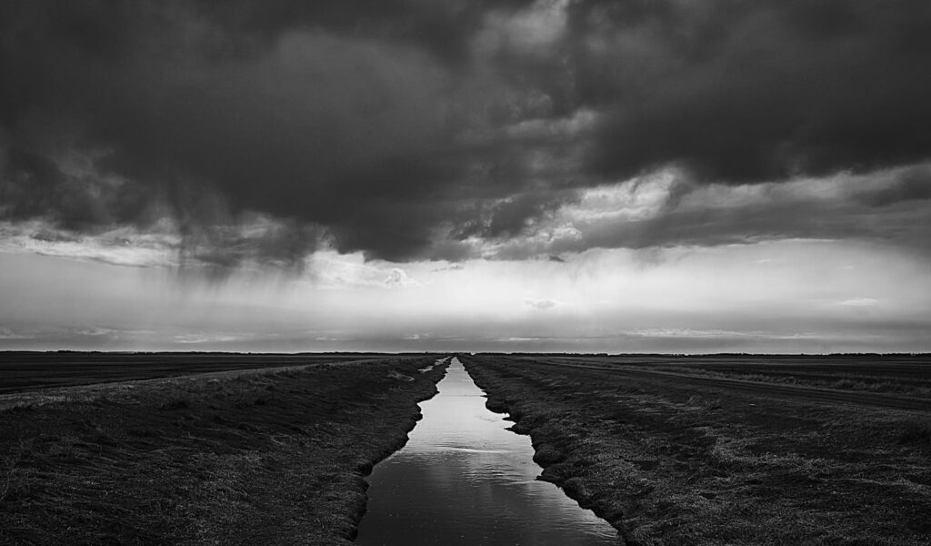 Dark storm clouds over a drainage ditch on the prairie