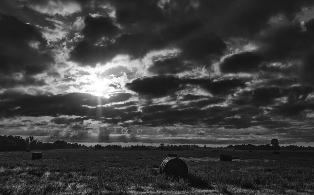 Sun breaking through dark clouds over hay bales