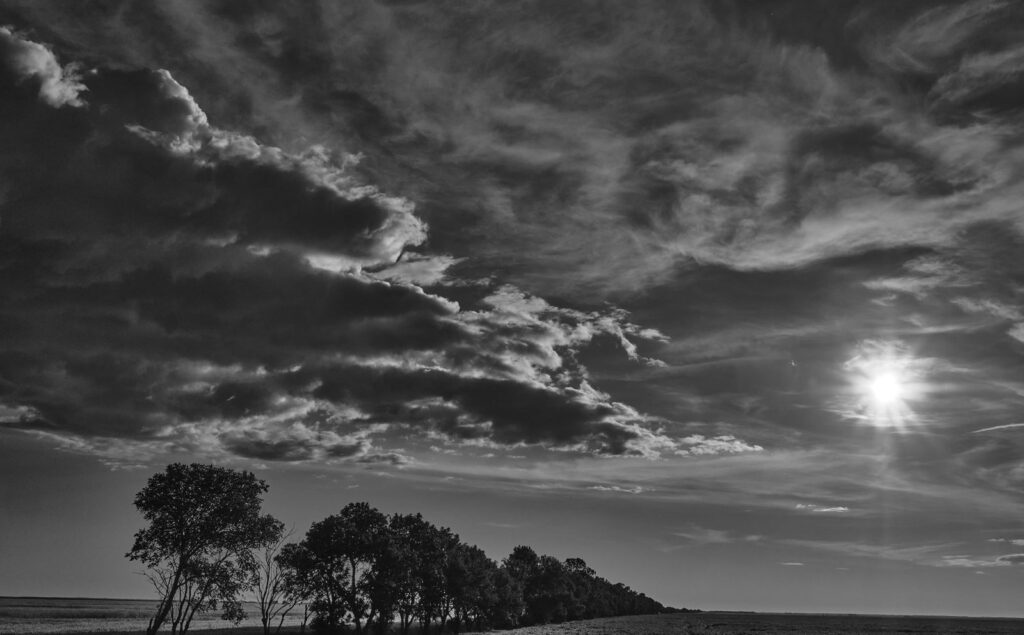 Sun peeking through broken clouds over a tree line