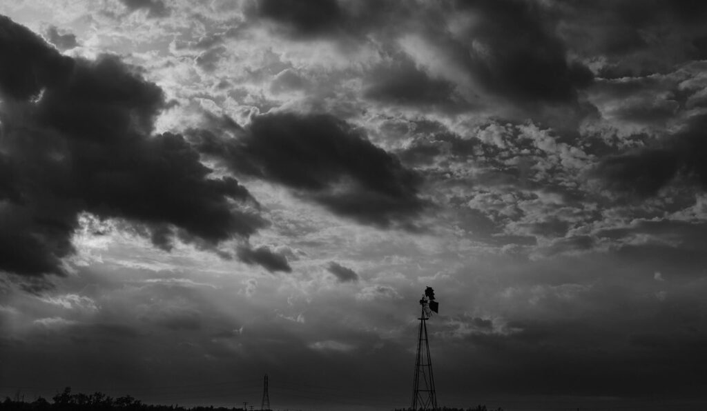 Storm clouds over a windmill and gravel road