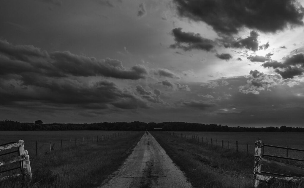 Dark clouds above a fenced road in the field