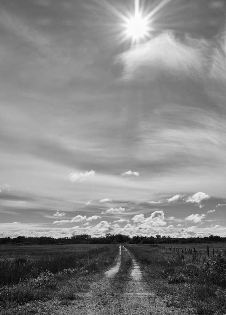 The sun high in a cloudy sky over a country track