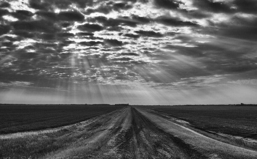 Sunbeams and mottled clouds over a farm road
