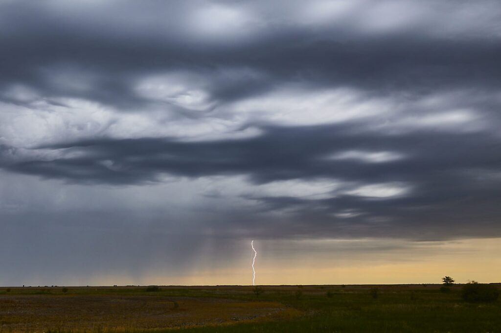 Layered grey storm clouds with lightning on the horizon over flat prairie