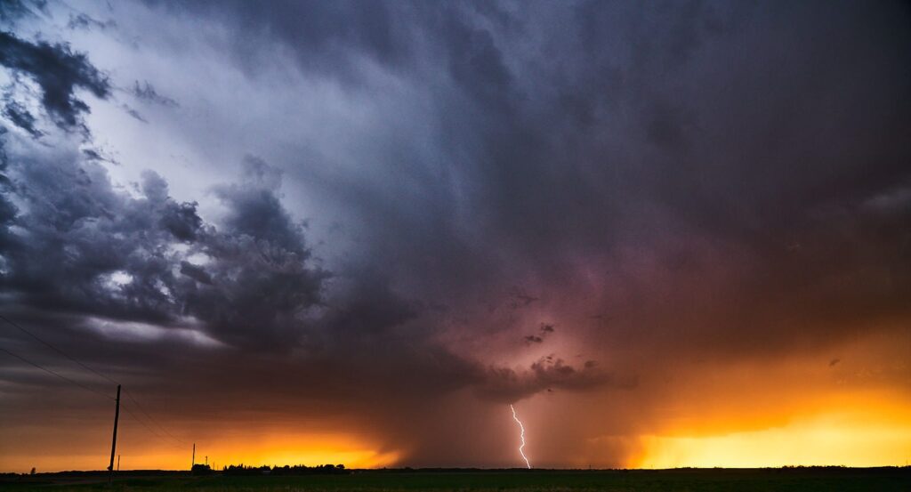 Dark storm clouds and lightning above a golden sunset horizon