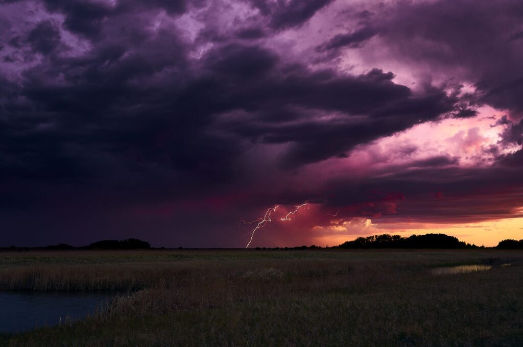 Purple storm clouds with lightning over a prairie slough
