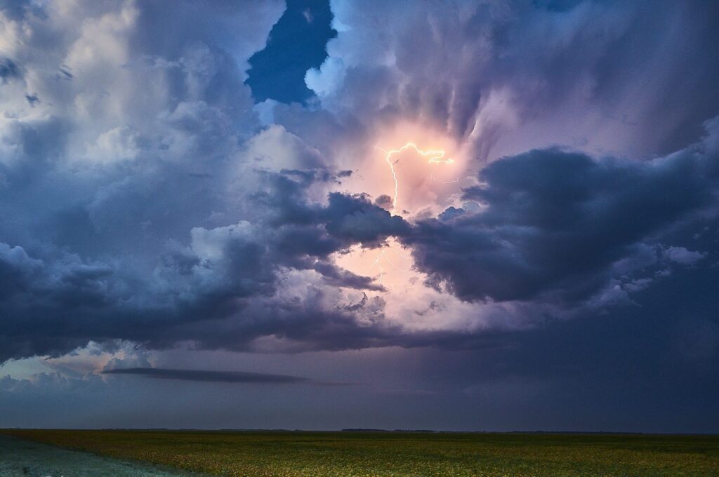 Blue thunderstorm clouds with a glowing break in the centre over a green field