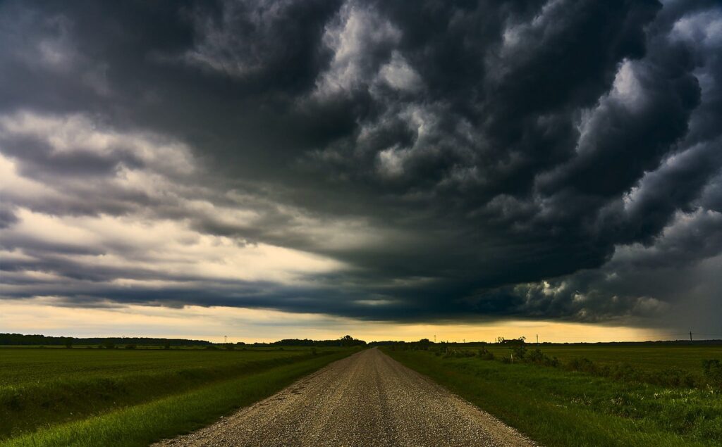 Dark green-tinted storm cloud over a gravel road and green field