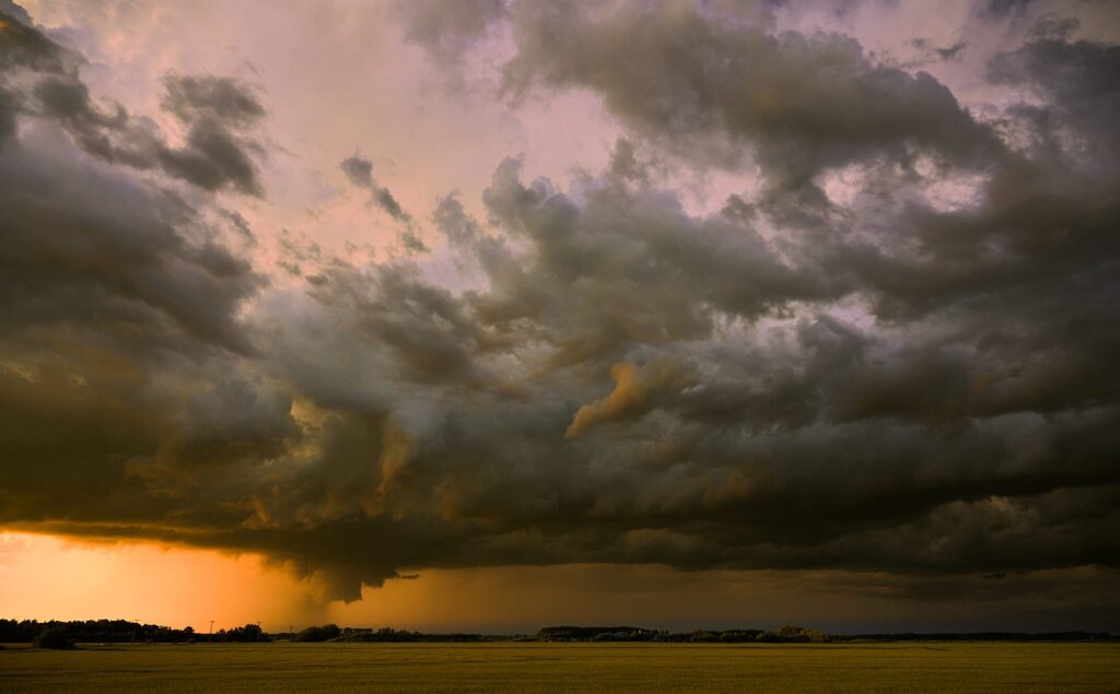 Low storm cloud trailing rain over a field at sunset