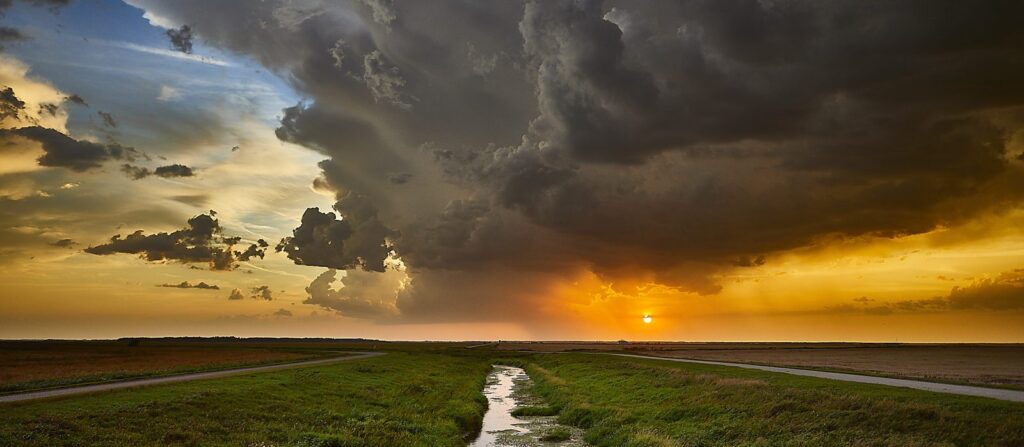 Dark storm cloud over a prairie field with a golden sunset glow