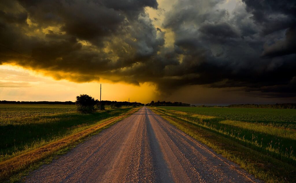 Dark storm clouds over a gravel road and a golden sunset