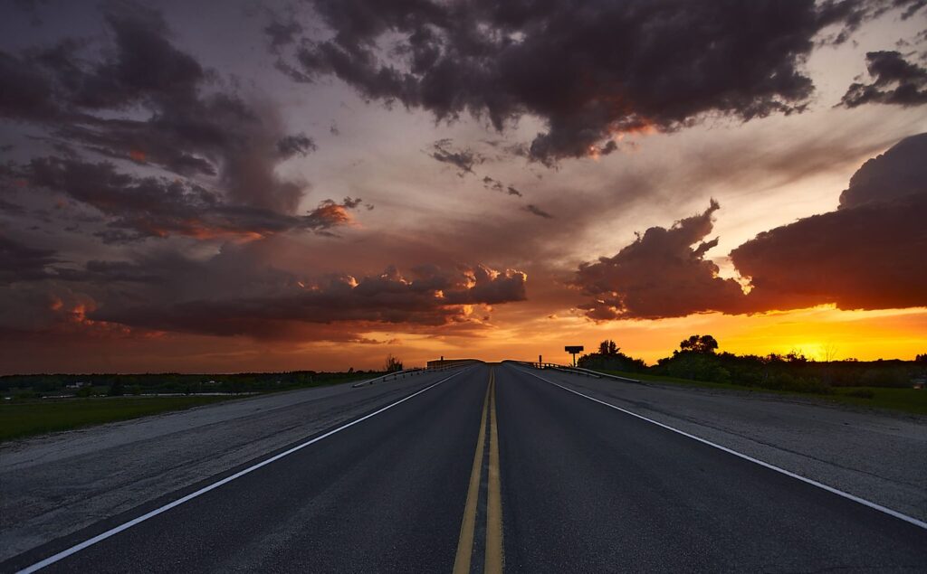 Storm clouds lit red and orange over a paved highway