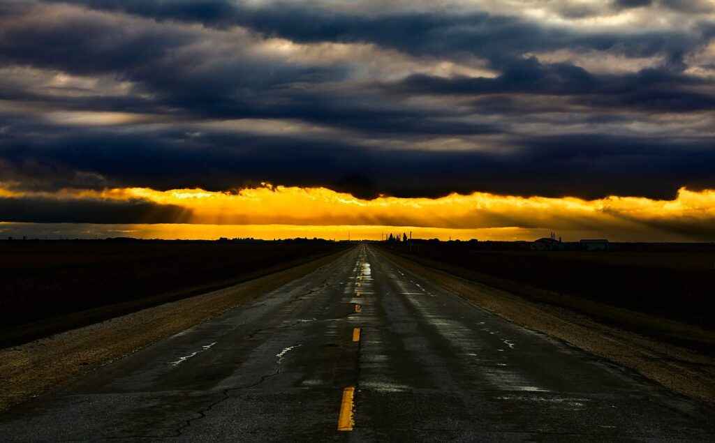 Dark band of cloud over a golden horizon and a wet highway